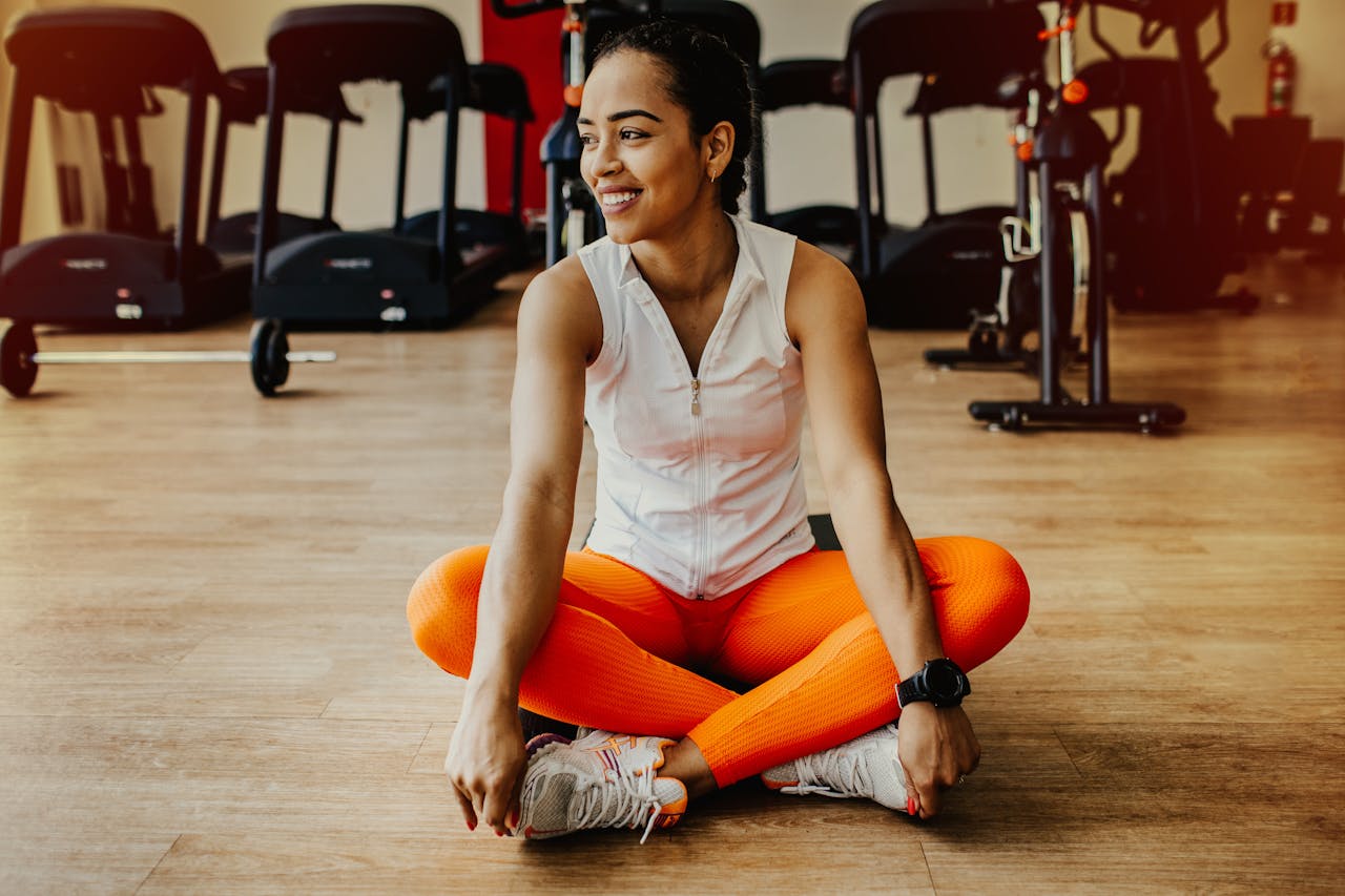 services-03 Confident woman in bright workout attire smiling while sitting in a gym.